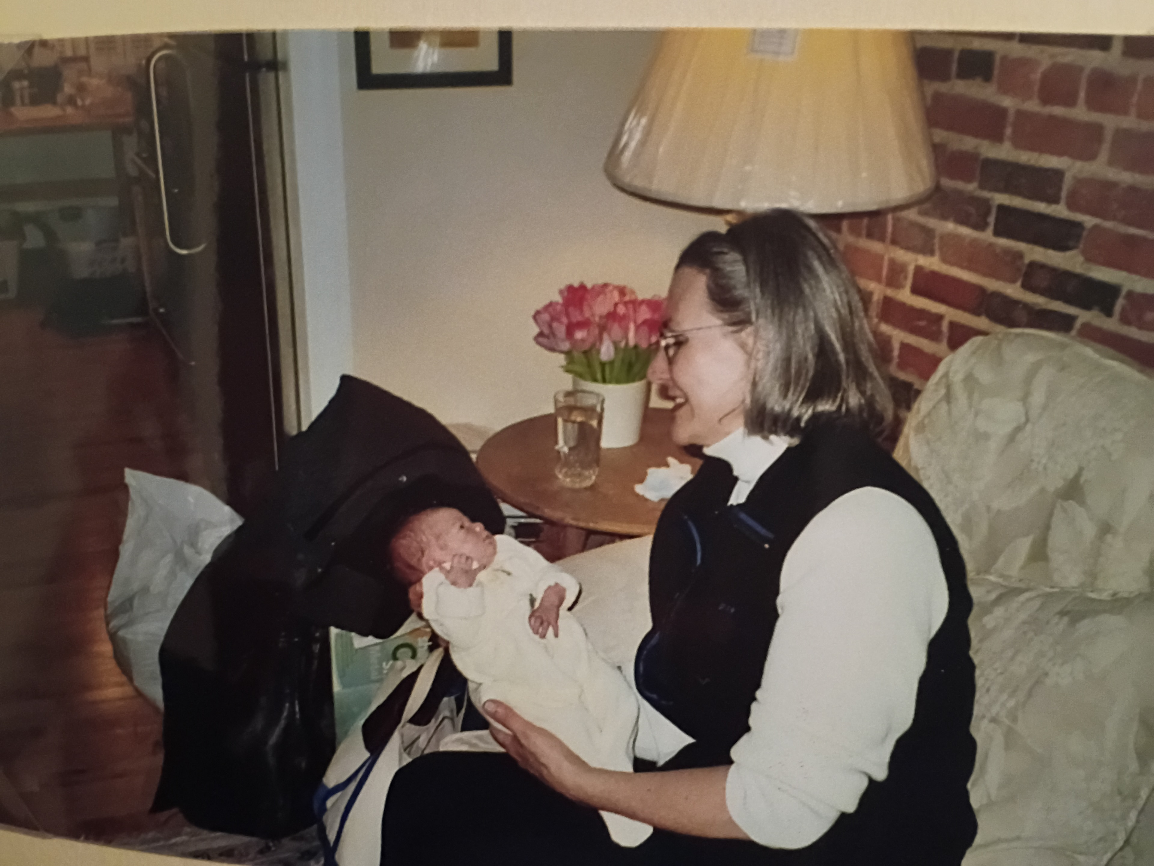 Martha holding my newborn daughter, smiling down at her, with pink tulips on the table behind them